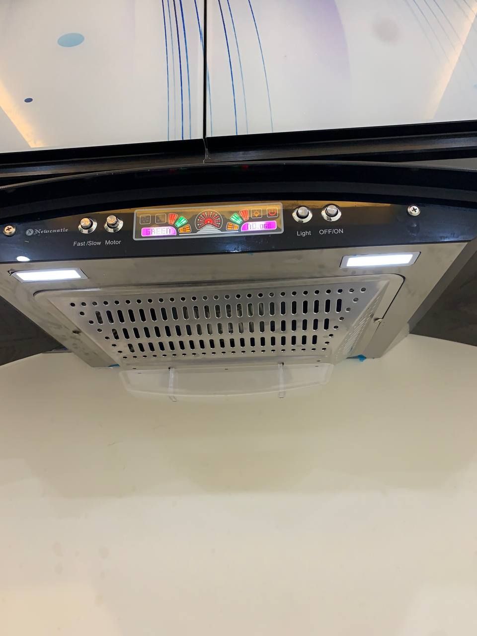 Eine Decke mit einem Lüftungsgitter und einer Bedieneinheit mit Lampen und Motorgeschwindigkeitseinstellung.