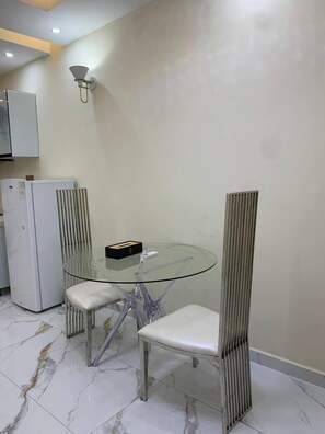 A compact kitchen with a glass dining table, two chairs, and a refrigerator.