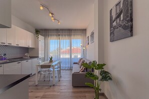 A modern kitchen with a dining area, a sofa, and a large window with curtains.