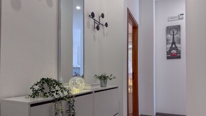 Un pasillo con una consola blanca, un espejo, un reloj en la pared y una puerta que da a otra habitación.