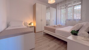 Un dormitorio con dos camas, un armario, una mesita de noche con lámpara y una ventana con cortinas.