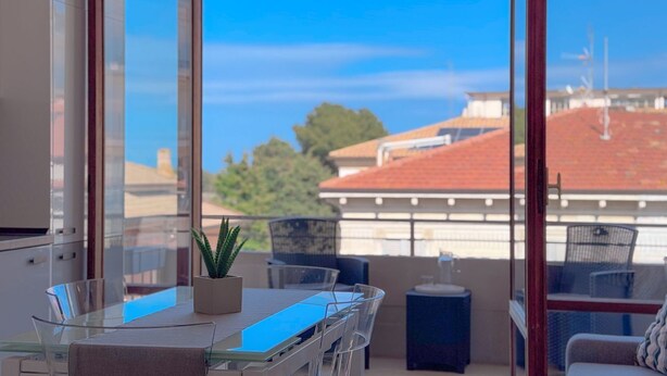 Un balcón con una mesa de vidrio, sillas y una planta en maceta.