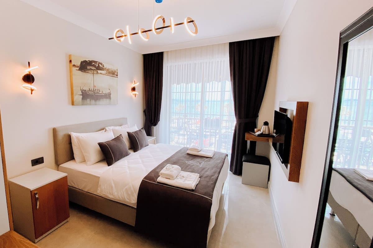 A modern hotel room with a large bed, a bedside table, a wardrobe, a flat-screen TV, and a city view.