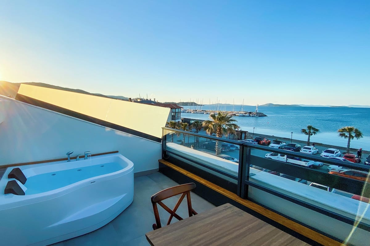 A balcony with a jacuzzi, a view of the sea, and parked cars.