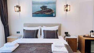 A hotel room with a bed, two bedside tables, a nightstand, a coffee maker, a telephone, and a painting of a coastal landscape.