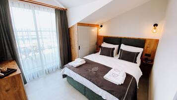 Ein Hotelzimmer mit Bett, Holz-Kopfteil, Nachttisch und einem Fenster mit Vorhängen.
