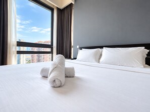Une chambre d’hôtel avec un grand lit, une vue sur les immeubles par la fenêtre et un lit parfaitement fait, avec une serviette roulée posée dessus.