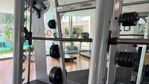 Un gimnasio con equipo de levantamiento de pesas, cintas de correr y un espejo que refleja el interior.