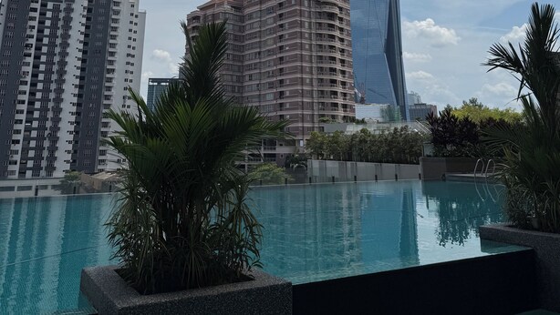 Un edificio moderno con un diseño único, una piscina rodeada de palmeras y otros edificios aledaños.