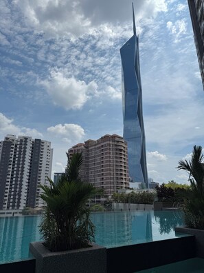 A modern building with a unique design, a swimming pool with palm trees, and other surrounding buildings. - Swiss Garden Residences by Roomy (Kuala Lumpur)