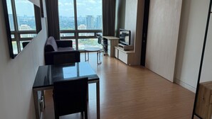 Una sala de estar moderna con un sofá, una mesa de comedor y un televisor. Amplias ventanas ofrecen vistas a la ciudad.
