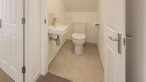 Een smalle badkamer met toilet, wastafel en een klein spiegel.