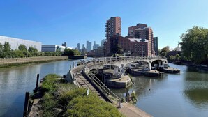 Een pad langs de rivier met een brug, een stadsachtergrond en een kalme rivier.