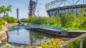 Een rivier met een blauwe brug, een stadion en een hoge constructie op de achtergrond.