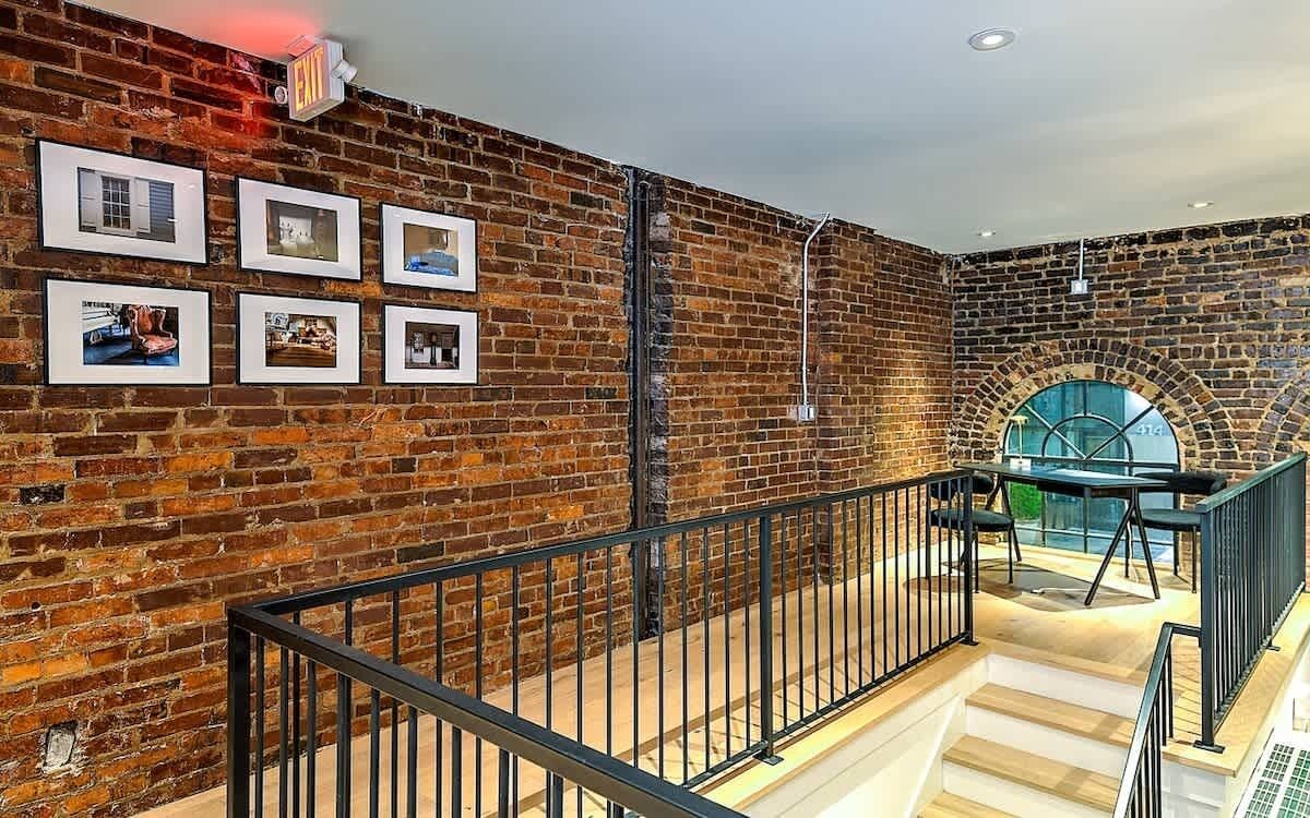 A staircase with a brick wall and framed pictures, leading to a seating area with a view of a circular window.