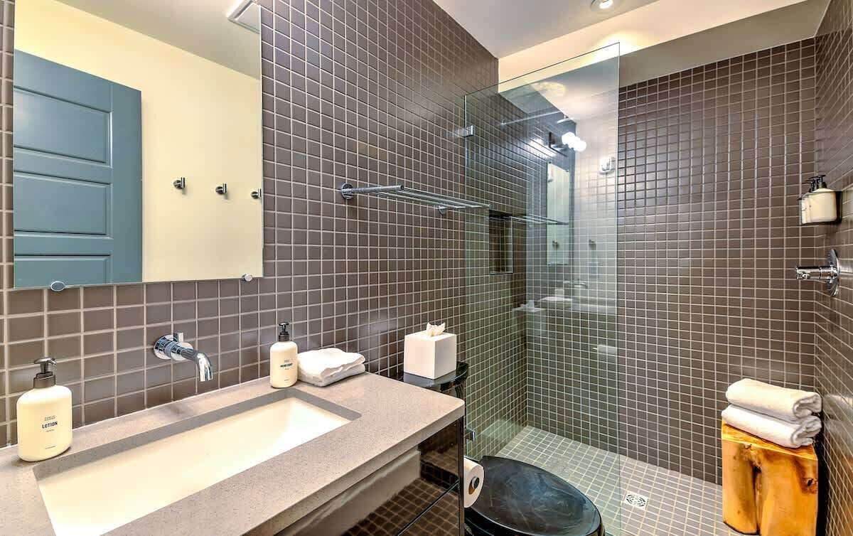 Un baño moderno con un espejo grande, un lavabo y una ducha con mampara de vidrio.