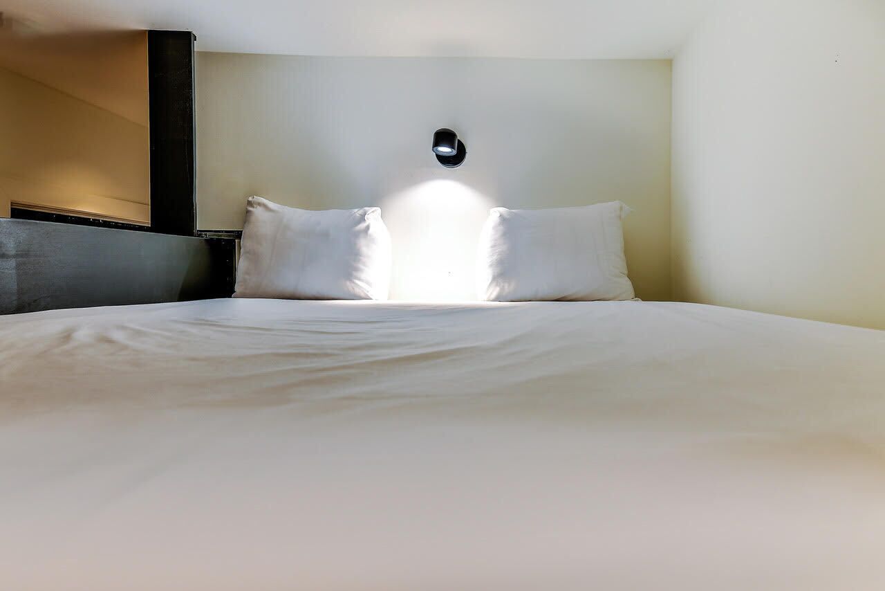 Habitación de hotel con una cama grande, cabecero e iluminación montada en la pared.