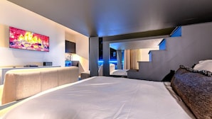 Une chambre d’hôtel moderne dotée d’un grand lit, d’un bureau avec une chaise, d’un téléviseur à écran plat et d’une salle de bain visible à travers une porte ouverte.