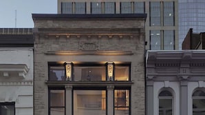 Un bâtiment historique doté d’une façade en pierre, de grandes fenêtres et d’une entrée imposante avec une porte noire.