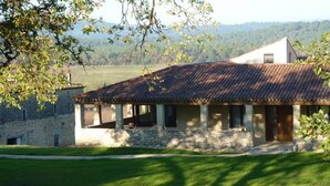 A stone house with a tiled roof, a porch, and a view of the surrounding countryside.
