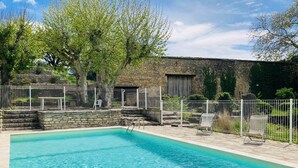 A rectangular swimming pool with clear blue water, surrounded by a stone wall and a white metal fence.