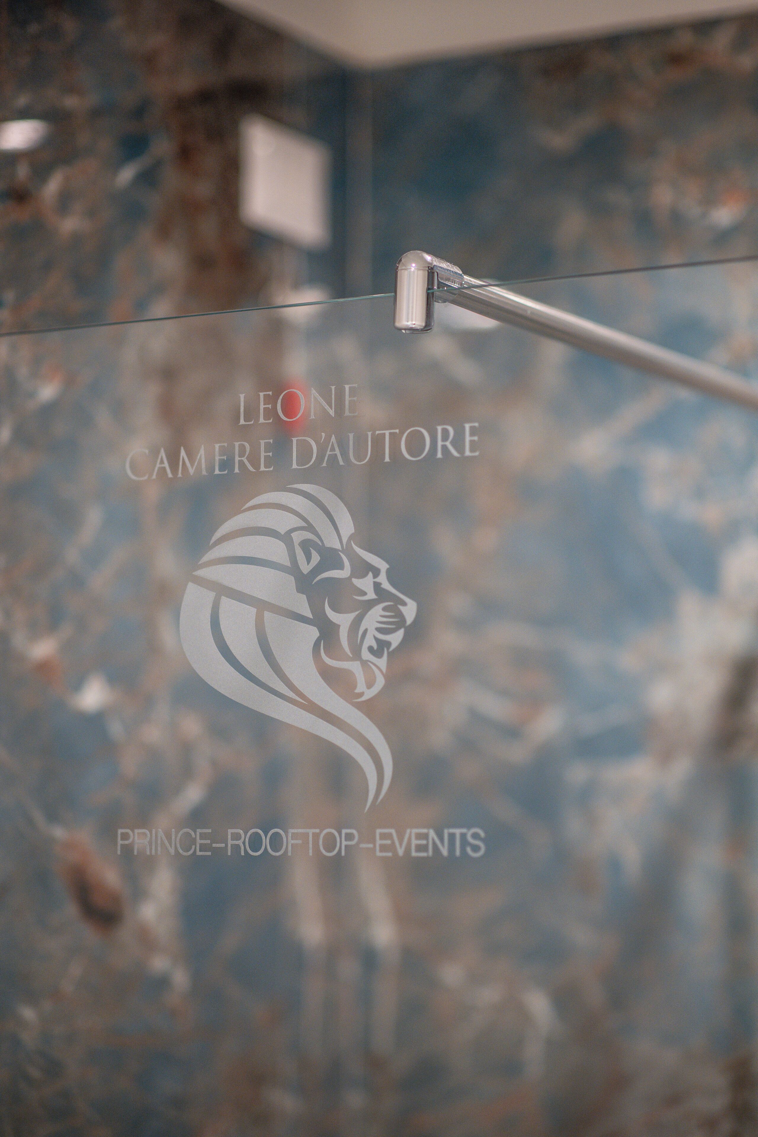 Lasinen sermi, jossa on logo ja teksti: ”LEONE CAMERE DAUTORE PRINCE-ROOFTOP-EVENTS”.