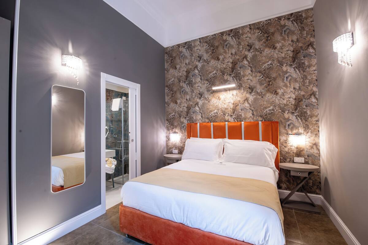 Ein modernes Schlafzimmer mit einem großen Bett, einem Spiegel und einem durch eine offene Tür einsehbaren Badezimmer.
