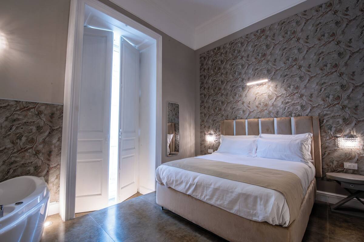Ein Schlafzimmer mit einem großen Bett, einem Nachttisch, einer Wandleuchte und einem Badezimmer mit einer Badewanne.