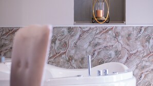 Ein modernes Badezimmer mit Marmor-Spritzschutz, einer weißen Badewanne und einer goldfarbenen Leuchte über dem Spiegel.
