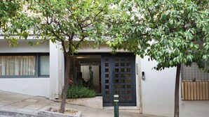 A building entrance with a dark door, steps leading up to it, and a small tree in the foreground. - Acropolis Soul (Athens)