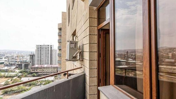 Un balcon donnant sur le paysage urbain, un sol en béton et une fenêtre à cadre en bois.