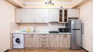 Une cuisine compacte avec des meubles de couleur bois clair, un lave-linge encastré, un réfrigérateur et un four à micro-ondes.
