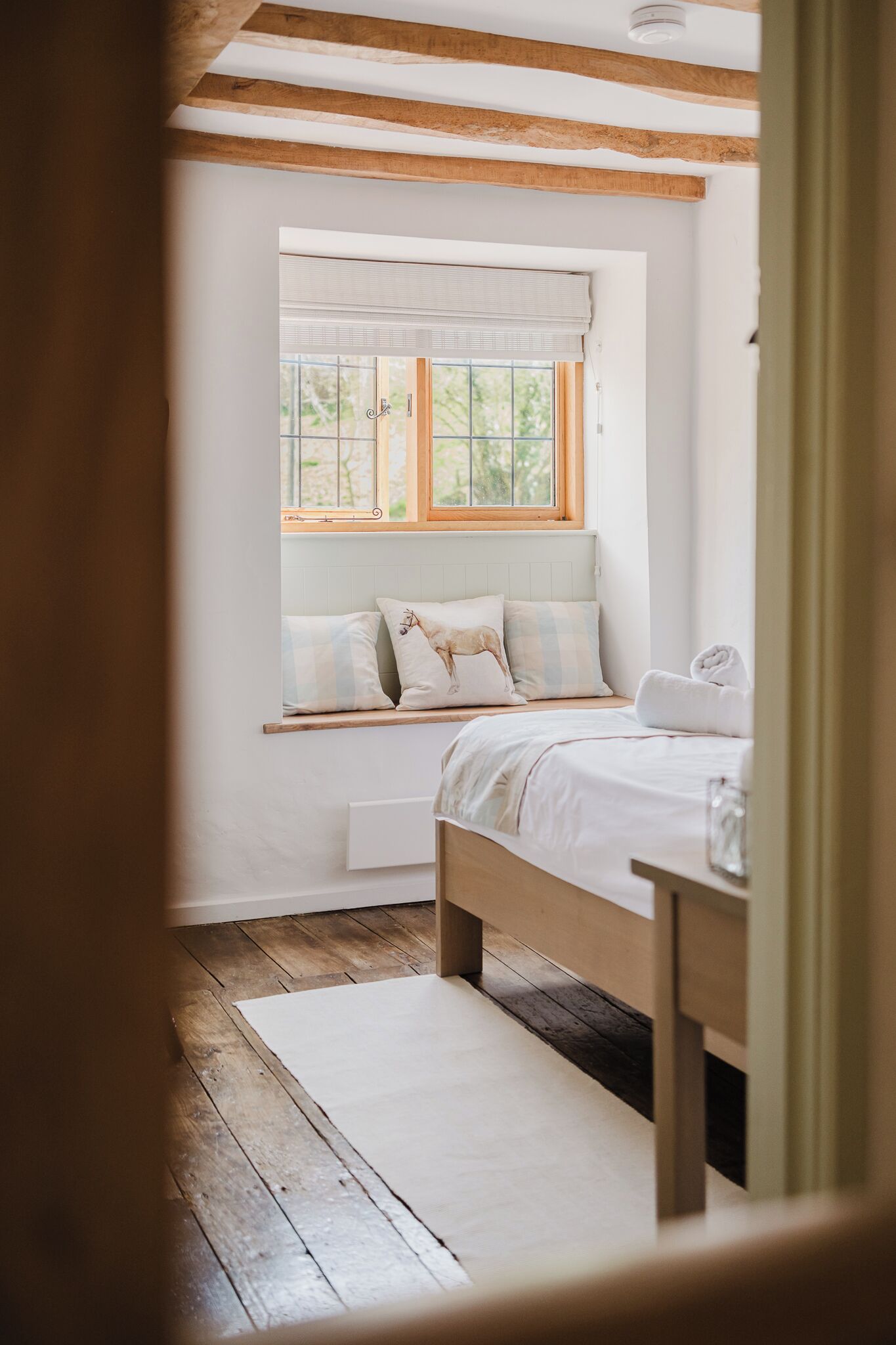 Un dormitorio con cama de madera, una ventana con persianas, una mesita de noche y una pared blanca.