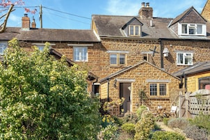 A stone house with a garden, a wooden fence, and a clear sky.