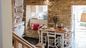 A rustic kitchen with stone walls, wooden beams, and a dining area with white furniture. - Sweetheart Cottage-Cosy 2BD in Cotswolds (Banbury)