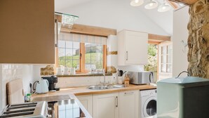 A kitchen with a stone wall, a washing machine, and a microwave. - Sweetheart Cottage-Cosy 2BD in Cotswolds (Banbury)