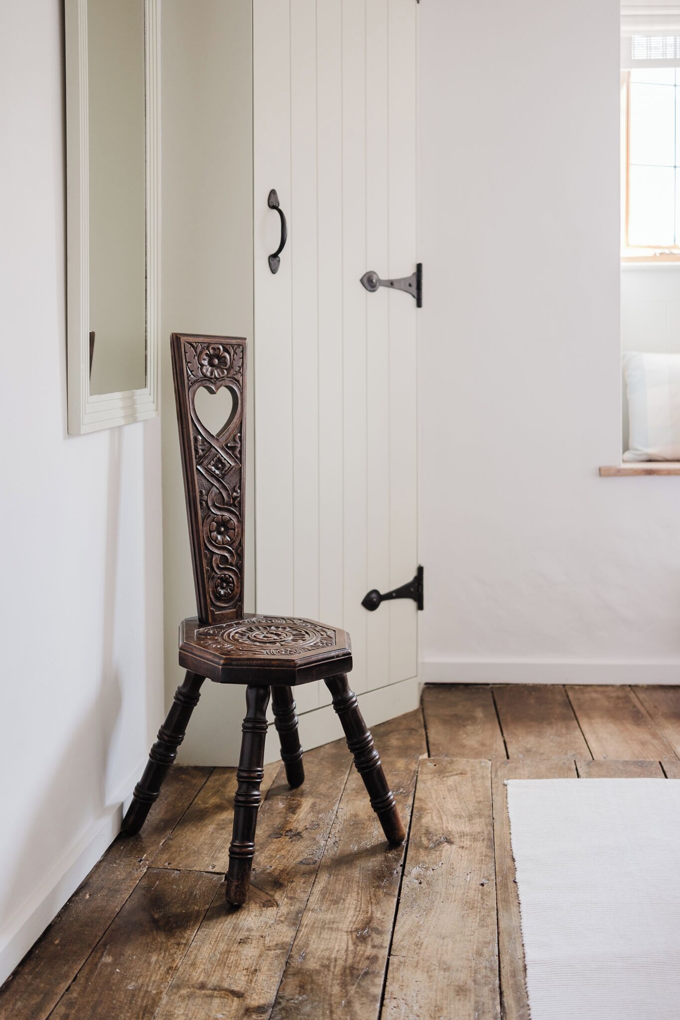 A wooden chair with intricate carvings in a room with white walls and wooden flooring.