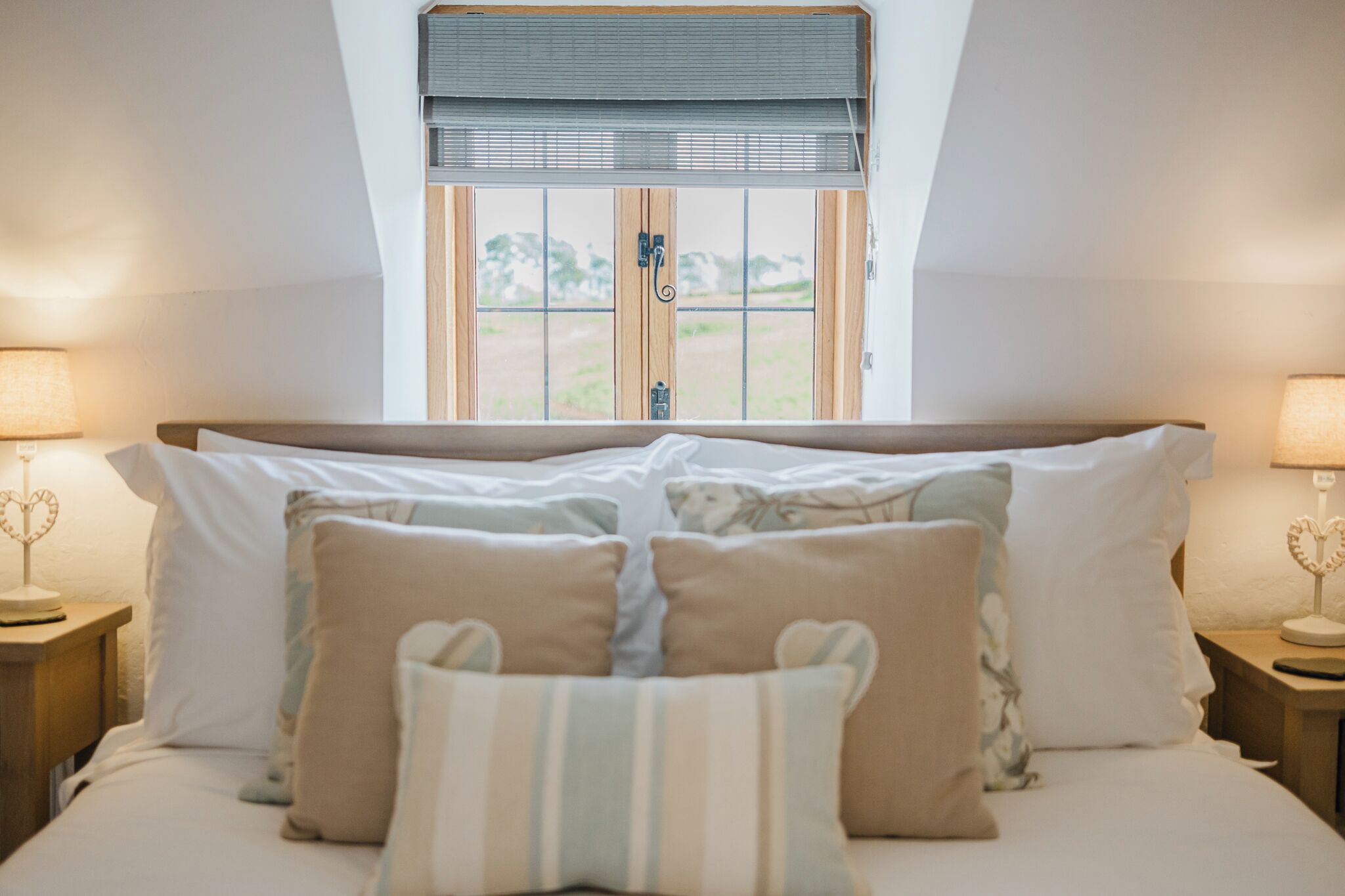 Ein Schlafzimmer mit Bett, Kissen, Nachttischen und einem Fenster mit Blick.