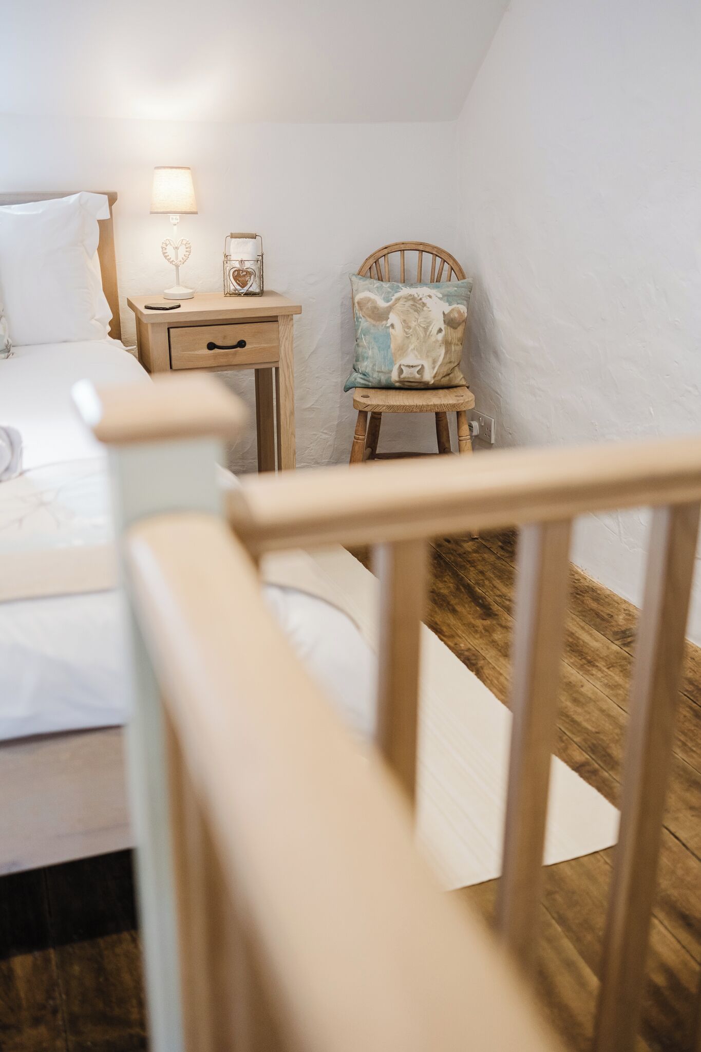 Una camera da letto con un letto, un comodino, una lampada e una sedia con un cuscino decorativo.