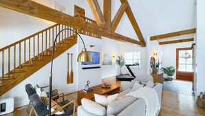 A spacious living room with a wooden staircase, a sofa set, a coffee table, and a piano. - Birch Beach Lake House-Hot tub/Sauna, Lake Access (Goderich)