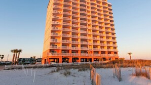 Ein Hochhaus-Hotel mit mehreren Balkonen, in Strandnähe mit Sand und spärlicher Vegetation.