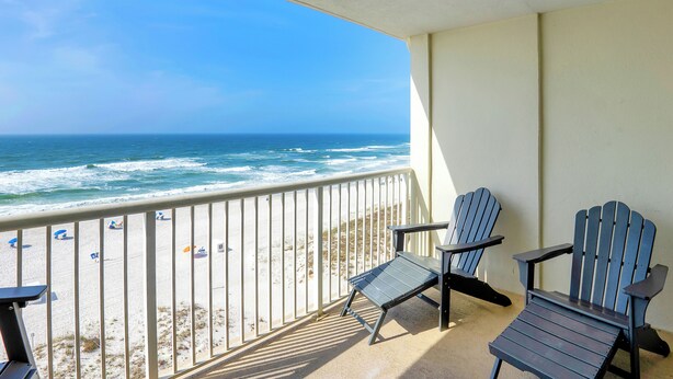 Ein Balkon mit zwei Adirondack-Stühlen mit Blick auf einen Strand mit Sonnenschirmen.