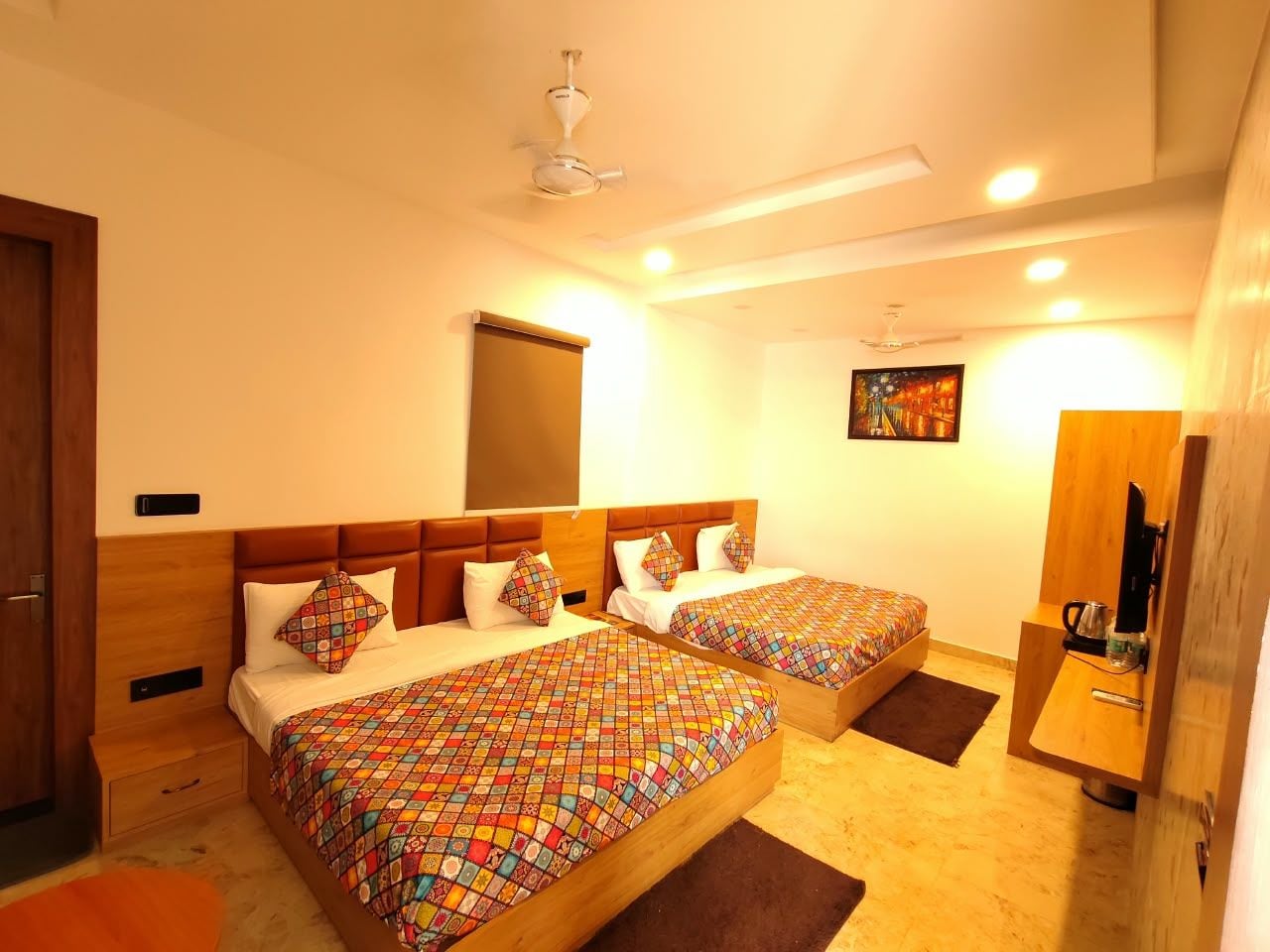 A hotel room with two beds, a ceiling fan, a painting on the wall, and a television on a wooden stand.