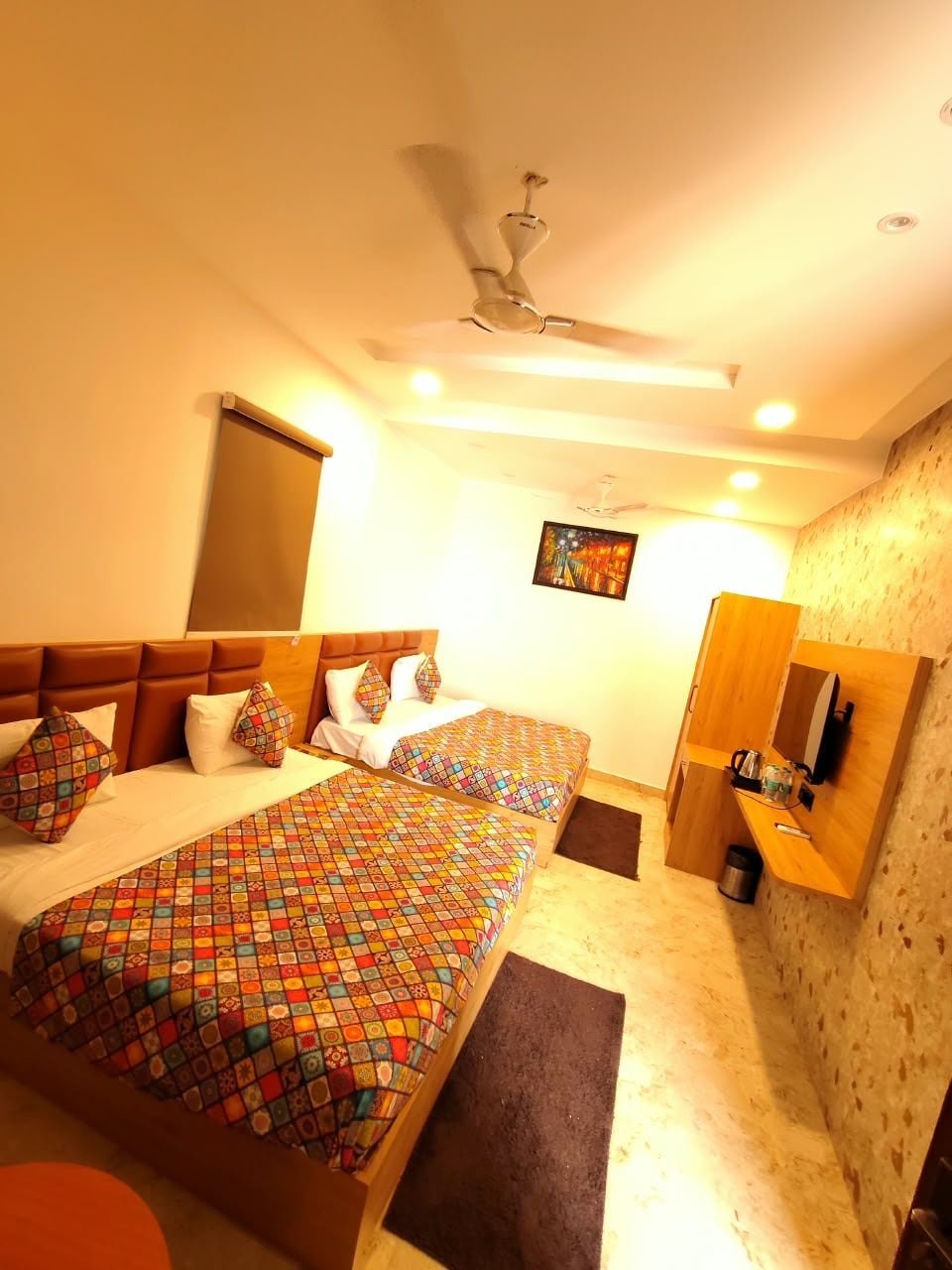 A hotel room with two beds, a ceiling fan, a painting on the wall, and a small desk with a mirror.