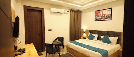 A hotel room with a bed, a desk, a chair, an air conditioning unit, and a painting on the wall.