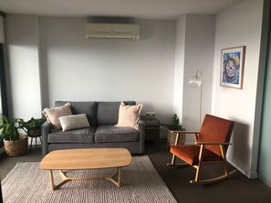 A modern living room with a grey sofa, a wooden coffee table, a rocking chair, and a floor lamp.