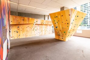 A climbing wall with various holds and a large, uniquely shaped structure in the foreground. - City Views Apt - FREE Parking , WIFI, Gym, + Pool! (Melbourne)