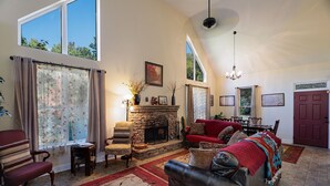 A spacious living room with a stone fireplace, a red sofa, and a dining area with a red door. - Foxwood Retreat, just minutes from Harrah's Casino in downtown Cherokee (Whittier)