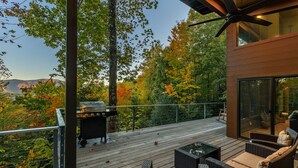 A deck with wicker furniture and a grill, overlooking a forested area.