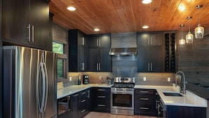 A modern kitchen with dark cabinetry, stainless steel appliances, and a wooden ceiling.